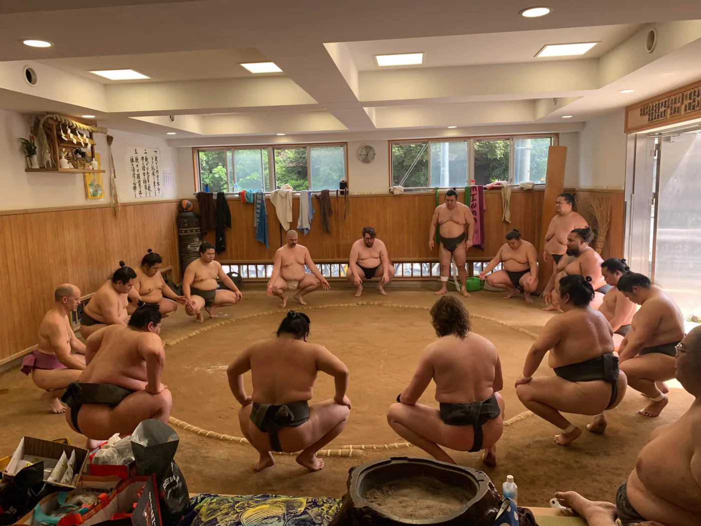 Wrestlers crouched in a circle around a clay dohyo in a practice stable