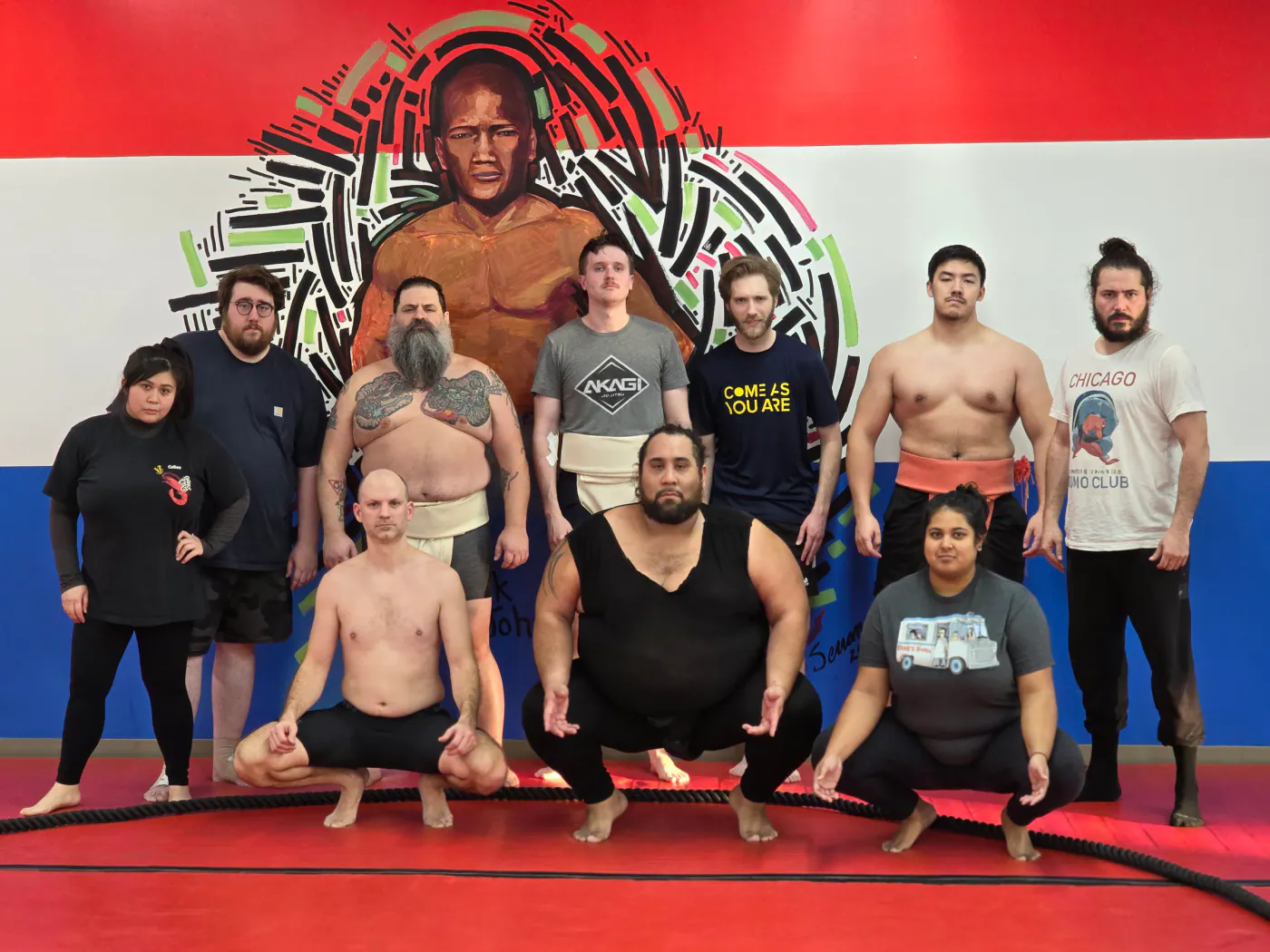 Chicago Sumo Club members posing in front of a mural of a sumo wrestler