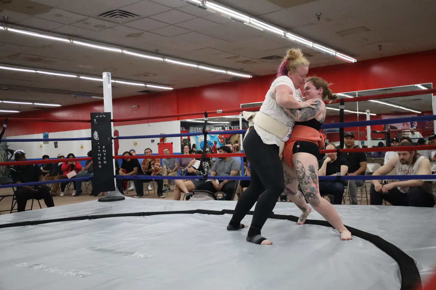 Two wrestlers locked in a clinch on the dohyo while spectators watch